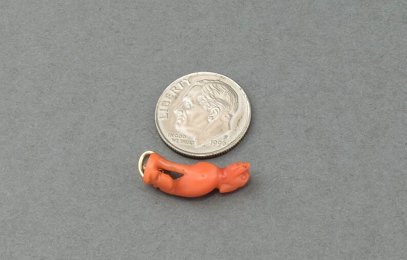 May include: A small, carved coral figurine of a dog, with a gold-colored loop for hanging. The figurine is about the size of a dime.