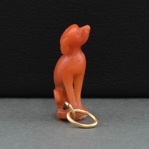 May include: A coral red carved dog figurine charm with a gold loop for attaching to a necklace or bracelet.