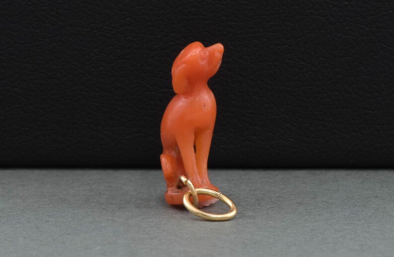 May include: A coral red carved dog figurine charm with a gold loop for attaching to a necklace or bracelet.