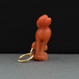 May include: A coral figurine of a dog with a gold jump ring attached. The figurine is a light orange color.