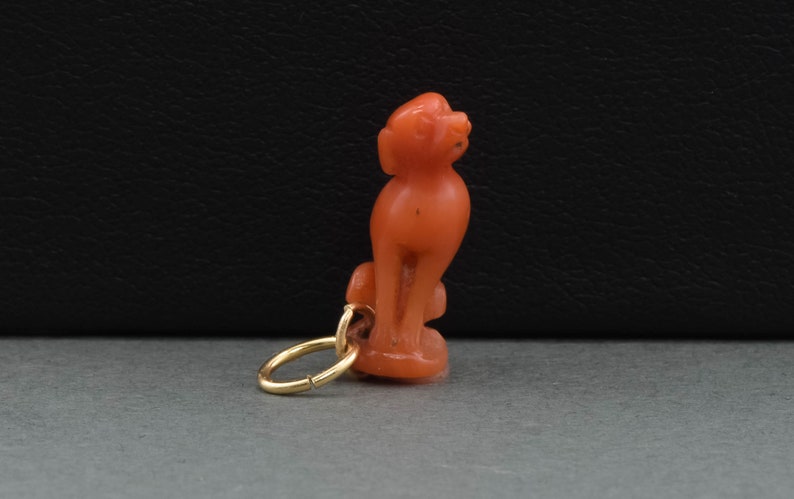 May include: A coral figurine of a dog with a gold jump ring attached. The figurine is a light orange color.