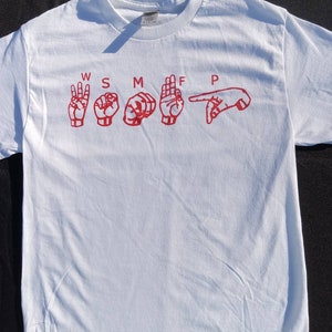 May include: White t-shirt with red letters spelling out "WSMFP" in American Sign Language.