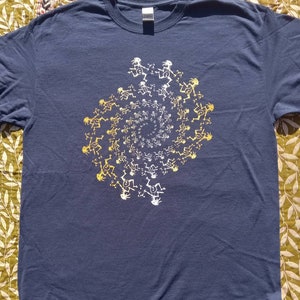 May include: Navy blue t-shirt featuring a spiral design of stylized figures in white and yellow. The figures appear to be dancing or in motion, creating a dynamic visual effect. The shirt is made of a soft, comfortable material.