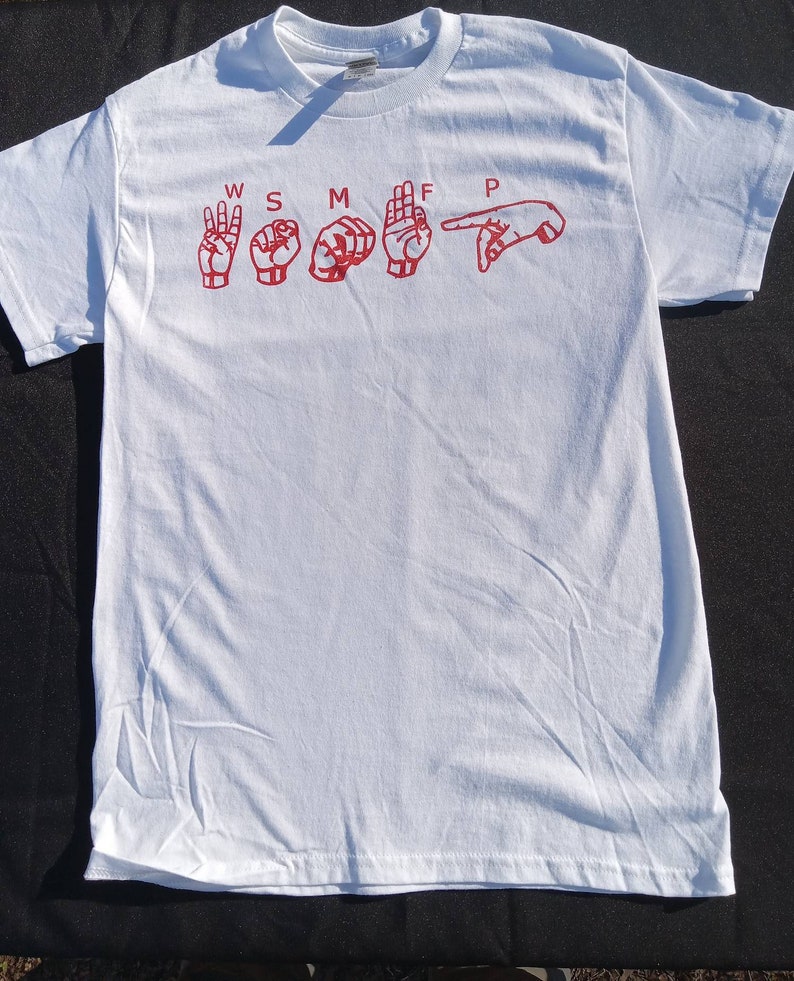 May include: White t-shirt with red sign language hand gestures spelling out "W S M T F P".