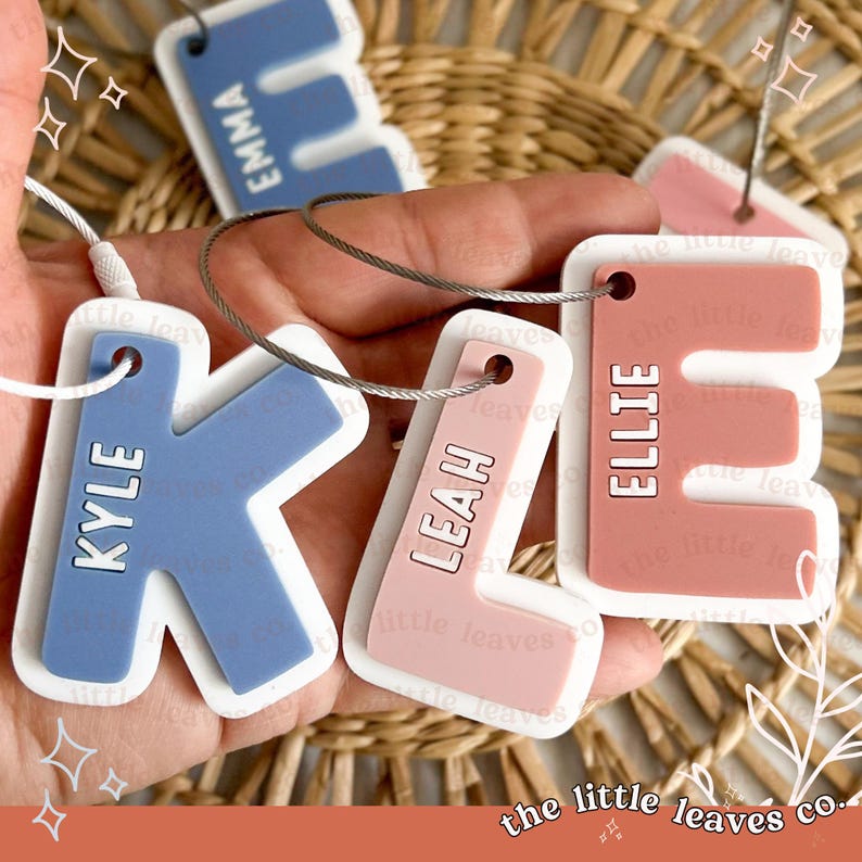 May include: Five colourful personalised keychains with names "Emma", "Kyle", "Leah", "Ellie", and "The Little Leaves Co."  The keychains are made of silicone and have a white border. The keychains are attached to silver metal rings.