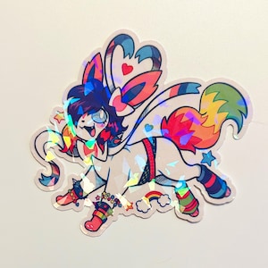 May include: A holographic sticker featuring a cartoon creature with a rainbow tail, wings, and accents. The creature has blue hair, a happy expression, and is adorned with stars, hearts, and a rainbow. The sticker has a white background.
