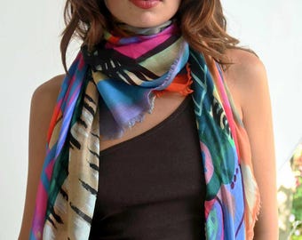 May include: A colorful abstract patterned scarf with blue, green, pink, orange, and beige colors. The scarf is tied around the neck of a person wearing a brown tank top.