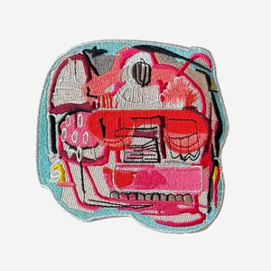 May include: Embroidered patch with an abstract design featuring shades of red, pink, and gray, outlined in a light blue border. The patch has a unique, artistic aesthetic, with intricate stitching and a variety of shapes and textures.