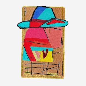 May include: Embroidered patch featuring an abstract design of a person wearing a hat. The patch has a brown background with a gold border. The hat is blue and red, and the person's face is pink. The design includes yellow, pink, and red elements.