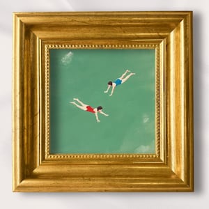 以下が含まれることがあります： 金色のフレームに入った正方形の絵画で、緑色の水の中を泳ぐ2人の人物が描かれています。一人は赤い水着、もう一人は青い水着を着ています。額装されたアートワークの上には「Lynn」および「100% Hand-Painted」というテキストが表示されています。
