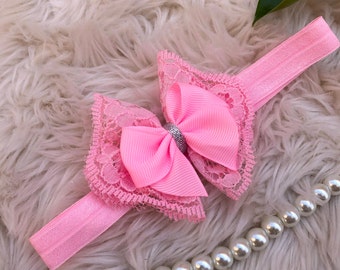 Puede incluir: Diadema rosa con un gran lazo rosa adornado con encaje y una pedrería plateada. La diadema es de elástico.