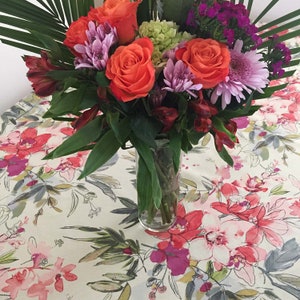Op de afbeelding: Een boeket met oranje, roze en paarse bloemen in een glazen vaas op een bloemenkleed. De bloemen omvatten rozen, anjers en alstroemeria.