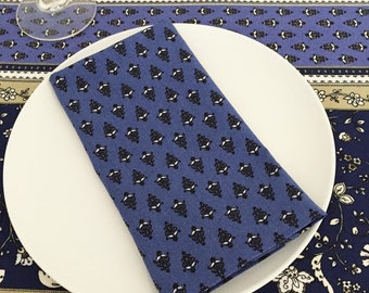 May include: A blue and white patterned cloth napkin folded on a white plate. The plate is on top of a blue and white patterned tablecloth.