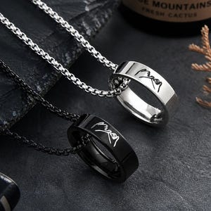 May include: Two ring pendants on box chains, one silver-toned and one black, each featuring a laser-engraved graphic of two hands making a pinky promise. The silver ring hangs from a silver chain, while the black ring hangs from a black chain.