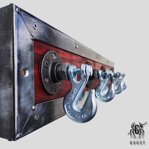 May include: A rustic industrial coat rack with a red wood backing and four metal hooks. The hooks are made from heavy duty chain links. The rack is mounted on a wall.