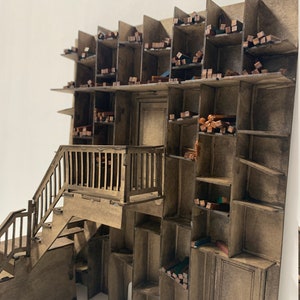 May include: A wooden model of a building with a staircase leading up to a balcony. The building has many shelves filled with small wooden blocks.