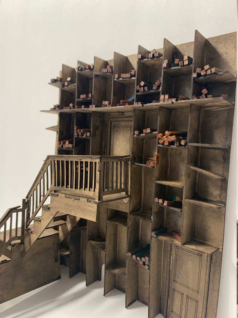 May include: A wooden model of a building with a staircase leading up to a balcony. The building has many shelves filled with small wooden blocks.