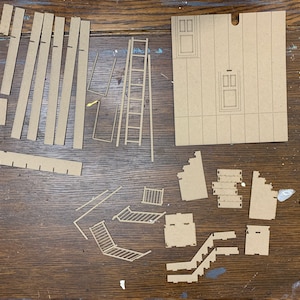 May include: A set of brown cardboard pieces for building a model house. The pieces include walls, doors, windows, stairs, and a ladder.