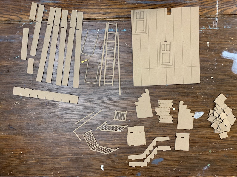 May include: A set of brown cardboard pieces for building a model house. The pieces include walls, doors, windows, stairs, and a ladder.