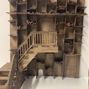May include: A miniature wooden model of a building with a staircase and a large wall of shelves. The shelves are filled with small wooden blocks of various colors.
