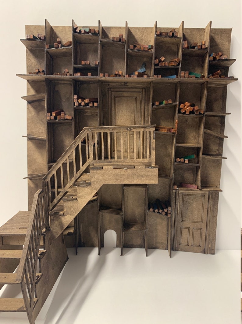 May include: A miniature wooden model of a building with a staircase and a large wall of shelves. The shelves are filled with small wooden blocks of various colors.