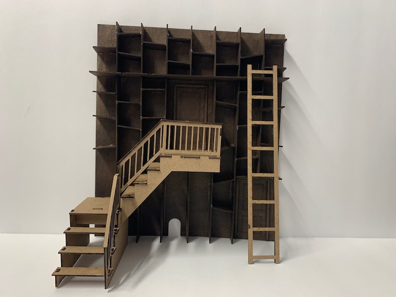 May include: A miniature model of a building with a brown facade, a wooden ladder, and a staircase leading to a small balcony. The facade is decorated with a series of rectangular cutouts, resembling shelves or windows.