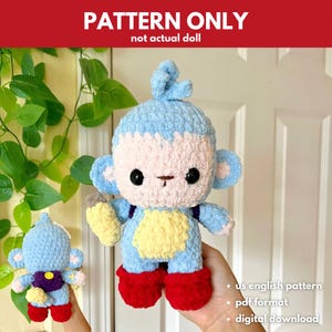 以下が含まれることがあります： かぎ針編みの猿の人形パターン。人形は青、ピンク、黄色、赤です。「PATTERN ONLY」の文字が上部にあります。人形は大きな黒い目を持ち、黄色のバナナを持っています。パターンはデジタルダウンロードです。