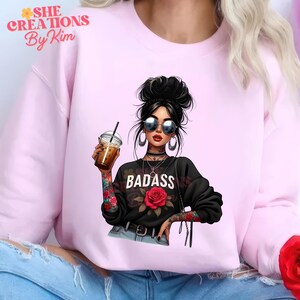 Puede incluir: Sudadera rosa con un gr&aacute;fico de una mujer con gafas de sol sosteniendo una taza de caf&eacute;. El gr&aacute;fico tambi&eacute;n incluye el texto "BADASS" y una rosa.