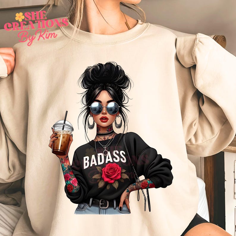 Puede incluir: Una sudadera beige con un estampado gr&aacute;fico de una mujer con un mo&ntilde;o, gafas de sol y tatuajes. La mujer sostiene una taza de caf&eacute; y tiene una rosa en su camiseta. El texto "BADASS" est&aacute; impreso en la camiseta.