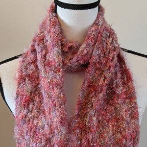 Pode incluir: Uma echarpe rosa e branca felpuda com um padrão de malha texturizado. A echarpe é feita de um material macio e felpudo e é perfeita para se manter aquecido no inverno.