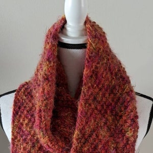 May include: A warm, fuzzy, red, orange and brown infinity scarf made of yarn. The scarf is on a white mannequin.