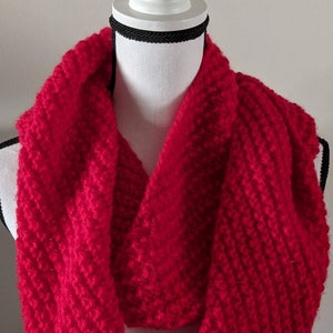 May include: A bright red knitted infinity scarf. The scarf is made from a soft, chunky yarn and is perfect for keeping warm in the winter.