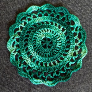 May include: A green crocheted doily with a circular design and a gradient of green shades.