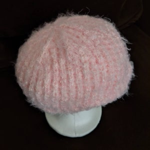 May include: A pink fuzzy knit beanie hat. The hat is soft and fluffy and has a ribbed texture.