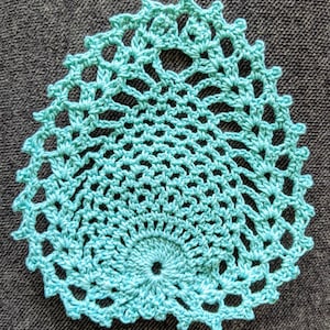 May include: A teal crocheted doily with a circular design. The doily has a delicate, lacy pattern and a small hole in the center.