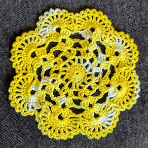 May include: A yellow crocheted doily with a white center. The doily is made with a delicate, intricate pattern.