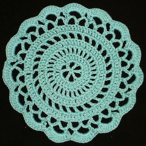 May include: A round, light blue crocheted doily with a scalloped edge. The doily features an open, lacy design with a central floral motif. The handmade piece is set against a black background.