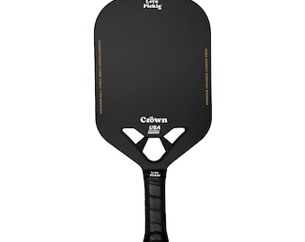 Könnte beinhalten: Schwarzer Pickleball-Schläger mit schwarzem Griff und goldener Beschriftung. Der Schläger hat eine große, offene Schlagfläche mit einem einzigartigen Design und den Text "Love Pickle" und "Crown USA" auf der Schlagfläche.