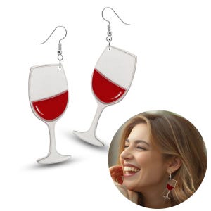 Pode incluir: Um par de brincos prateados em forma de taças de vinho, cada um com vinho tinto. Os brincos estão pendurados em ganchos prateados. As taças de vinho estão inclinadas.