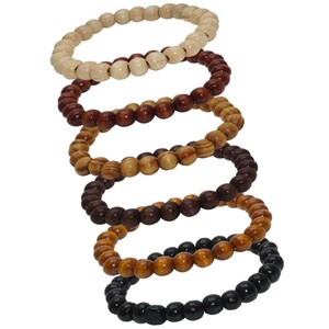 Könnte beinhalten: Satz von sechs Holzperlenarmbändern in verschiedenen Brauntönen, Beige und Schwarz. Die Armbänder sind übereinander gestapelt, wobei das schwarze Armband unten liegt.