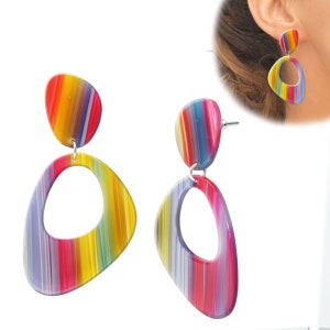 Könnte beinhalten: Ein Paar bunte gestreifte Ohrhänger mit einer großen ovalen Form und einer kleineren runden Form. Die Ohrringe sind aus Acryl und haben einen silbernen Haken.