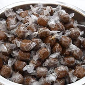 Op de afbeelding: Een kom gevuld met individueel verpakte bruine snoepjes. De snoepjes zijn verpakt in doorzichtig plastic en zijn in een willekeurig patroon gerangschikt.