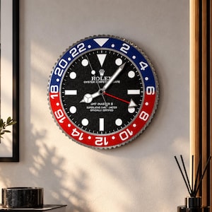 May include: A round wall clock featuring a black dial with white hour markers and the Rolex Oyster Perpetual Date GMT-Master II logo. The bezel is divided into blue and red sections with white numerals ranging from 2 to 22 in increments of two.