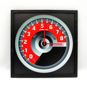 Peut inclure: Une horloge murale encadrée de noir avec un design de compteur de vitesse rouge et argent. Le cadran de l'horloge comporte les chiffres de 0 à 8 et le texte "x1000 / min".