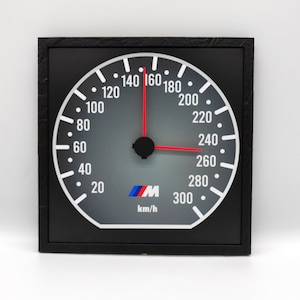 Könnte beinhalten: Ein schwarz-weißer Tachometer mit einem roten Zeiger und einem blau-roten "M"-Logo. Der Tachometer zeigt bis zu 300 km/h an.