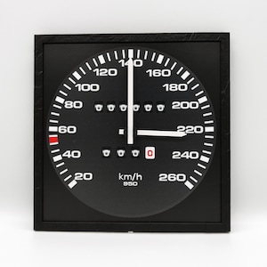 Op de afbeelding: Zwart-witte snelheidsmeter met een rode naald, die een snelheid van 60 km/h aangeeft. De snelheidsmeter heeft een zwart gezicht met witte markeringen en cijfers. Het gezicht is omgeven door een zwarte bezel met een zilveren rand. De snelheidsmeter is gemonteerd op een zwarte muur.