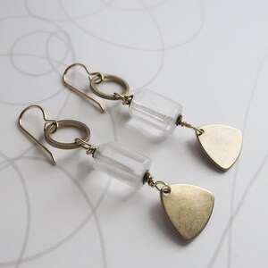 May include: A pair of gold-colored earrings with clear, rectangular beads and small, gold-colored, triangular pendants. The earrings have a simple design with a hook closure and a circular accent.