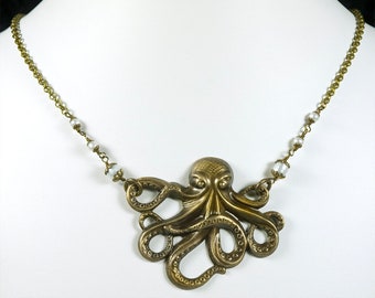 Op de afbeelding: Een gouden ketting met een gedetailleerde octopus hanger en witte parel accenten.