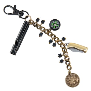 Op de afbeelding: Een multi-tool sleutelhanger met een zwarte fluit, een klein vouwmes en een kompas. De sleutelhanger heeft een bronskleurige ketting met zwarte vierkante kralen en een Sint-Christoffelmedaille. De sleutelhanger is bevestigd aan een zwarte metalen clip.