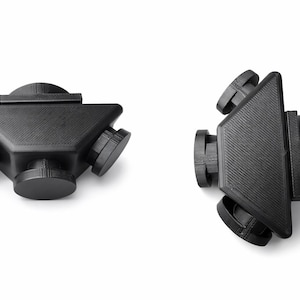 Può includere: Due oggetti neri di forma geometrica sono esposti su sfondo bianco. Gli oggetti hanno una superficie strutturata e un design triangolare con attacchi circolari. Un oggetto è posizionato orizzontalmente, l'altro è angolato.